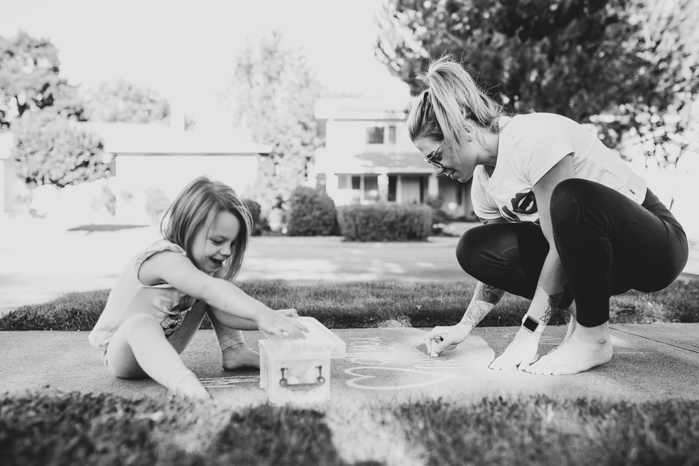 black and white picture of a little girl and her mom doodling with sidewalk chalk during the coronavirus pandemic in California