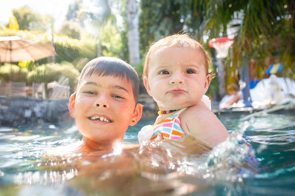 tween boy holding his baby girl cousin in a pool