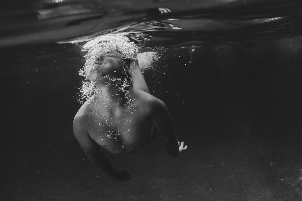 black and white underwater image of a child surfacing