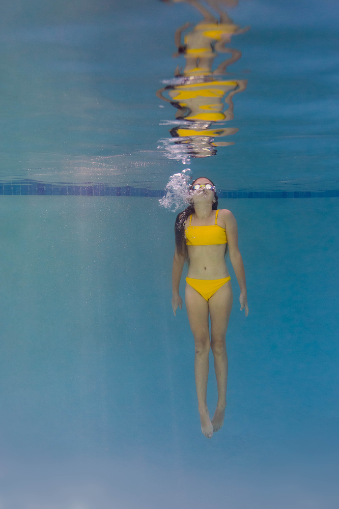 girl wearing goggles and yellow swimsuit in pool, bubbles